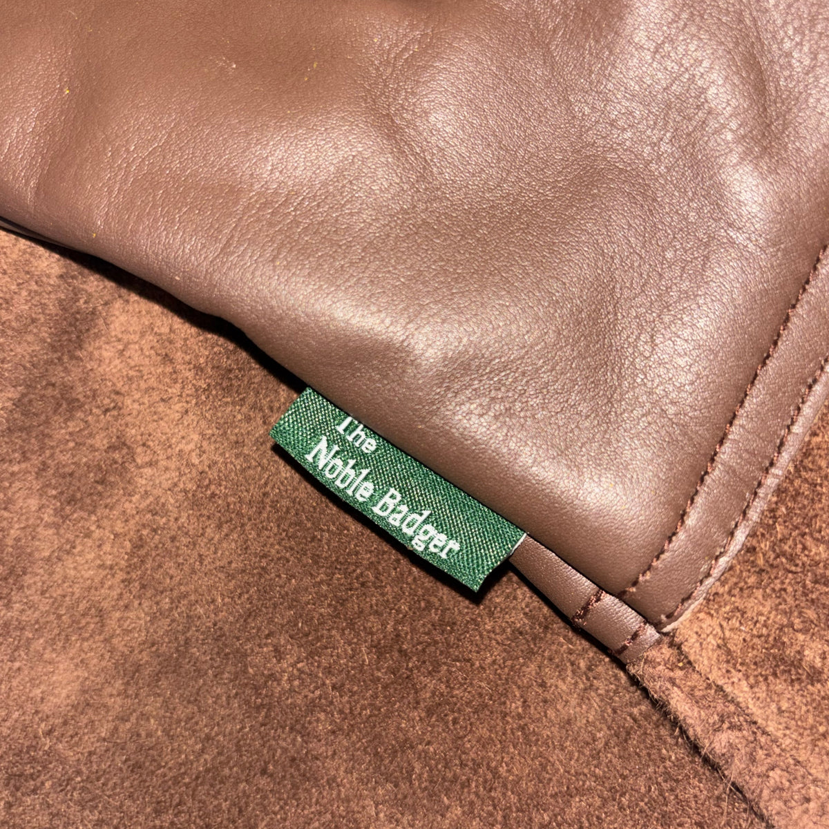Close-up of a brown leather product with a green label featuring 'The Noble Rider' branding.